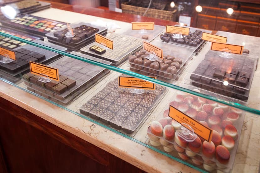 A glass display case filled with rows of assorted chocolates, including heart shaped, square, and round pieces, with descriptive labels.