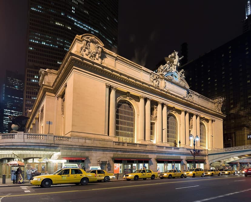 Exterior of Grand Central Terminal at night with the Glory of Commerce statues and clock, and yellow taxis on the street.