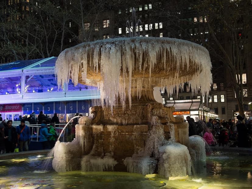 A large stone fountain, the Josephine Shaw Lowell Memorial Fountain, covered in icicles and ice formations at night in Bryant Park.