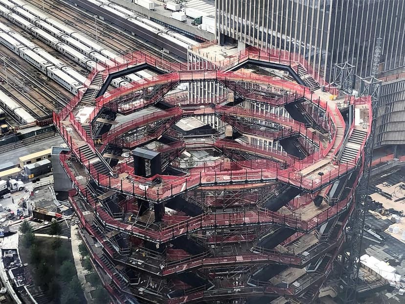 Aerial view of the Vessel sculpture under construction at Hudson Yards, featuring its complex staircases and red safety netting.