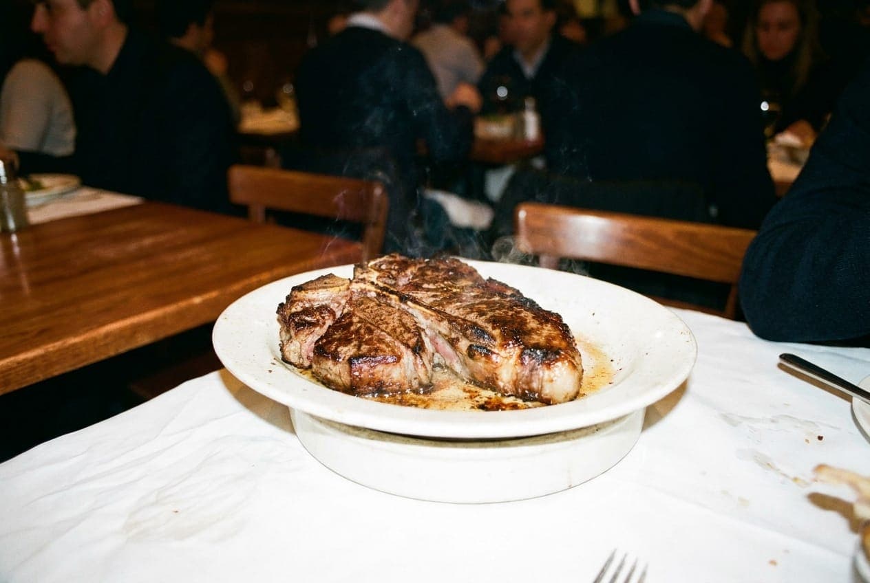 A sizzling porterhouse steak on a thick white ceramic plate in a classic New York dining room