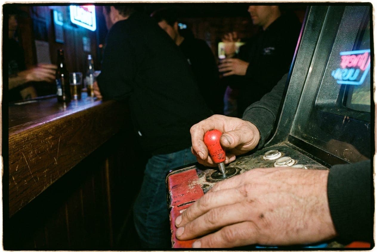 Hands playing a classic arcade game in a dark bar