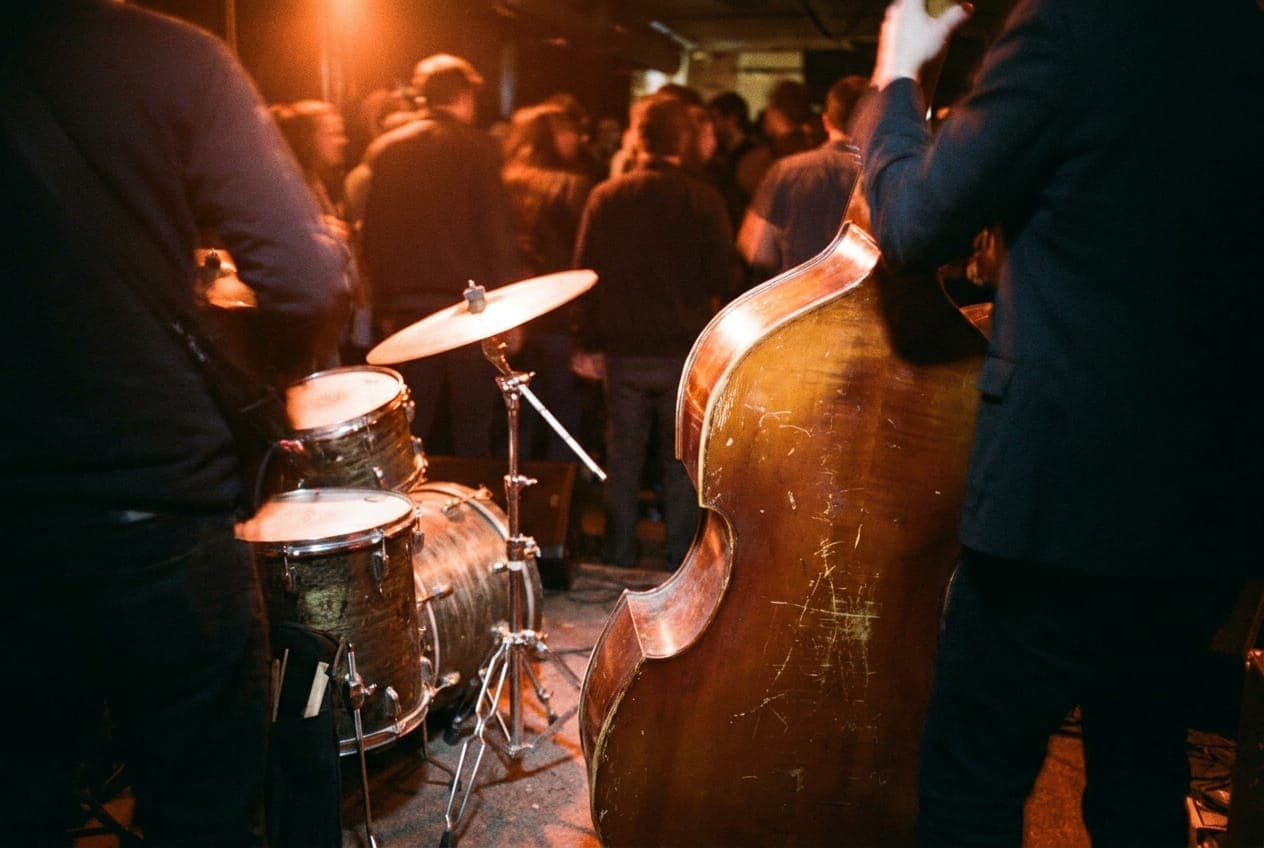 A worn upright bass and drum kit sitting on a dark stage in a downtown New York club