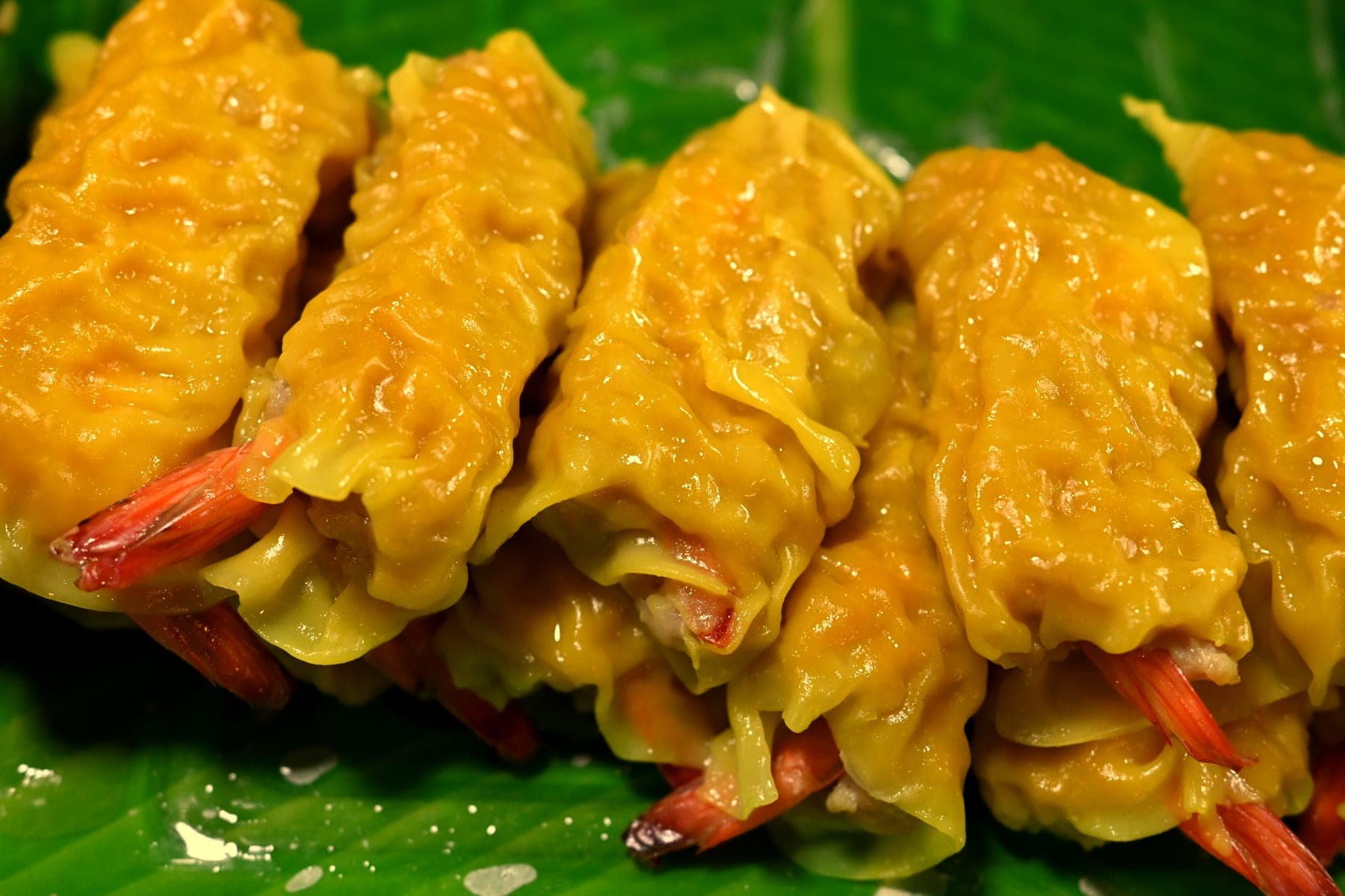 DFC 0301 Golden shrimp dumplings neatly arranged on a vibrant green leaf the crispy tails peeking out of glossy savory wrappers