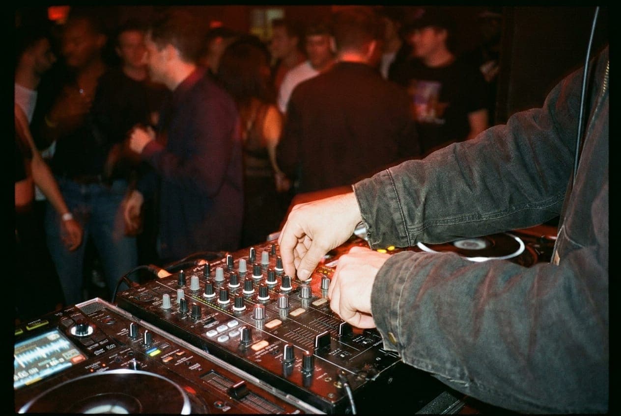 A DJ's hands adjusting a mixer in a dark, red-lit club