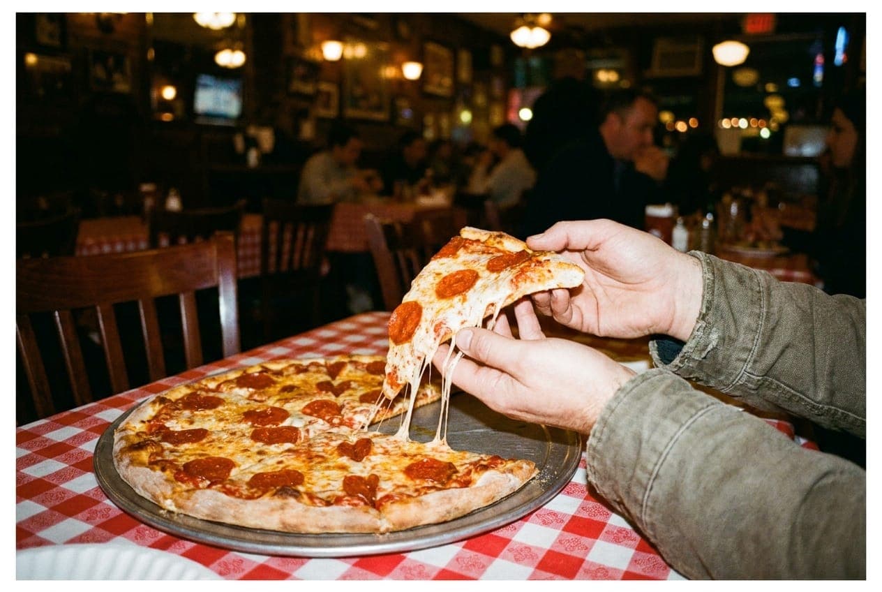 A close crop of hands lifting a slice of pizza in a dimly lit restaurant