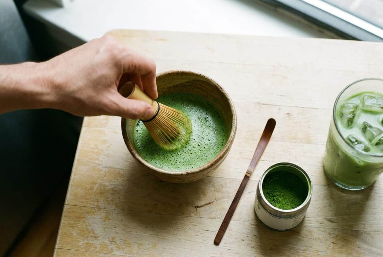A bowl of bright green matcha being whisked with a bamboo whisk
