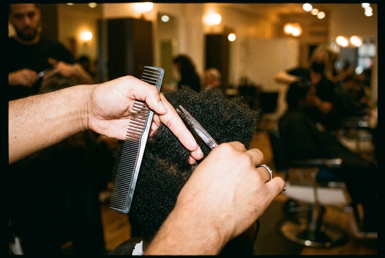A stylist's hands mid-snip, with scissors and a comb visible against a blurred background of a salon interior.