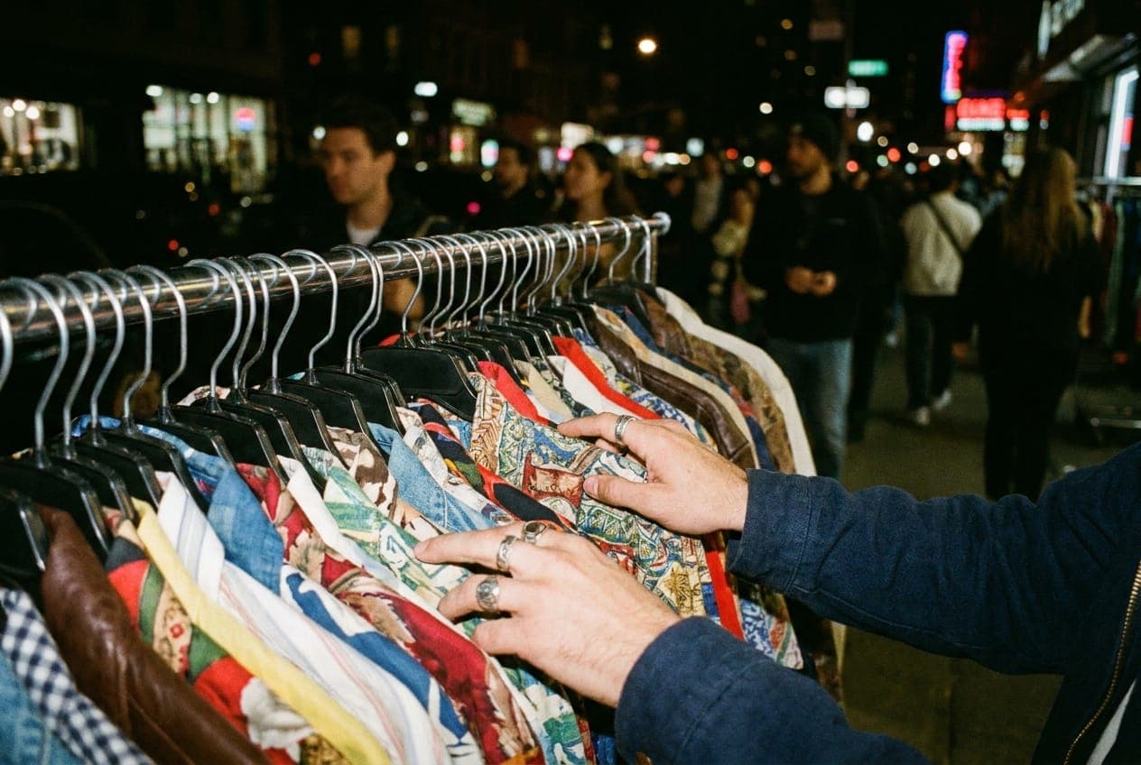 A hand flipping through vintage garments on a clothing rack at night.