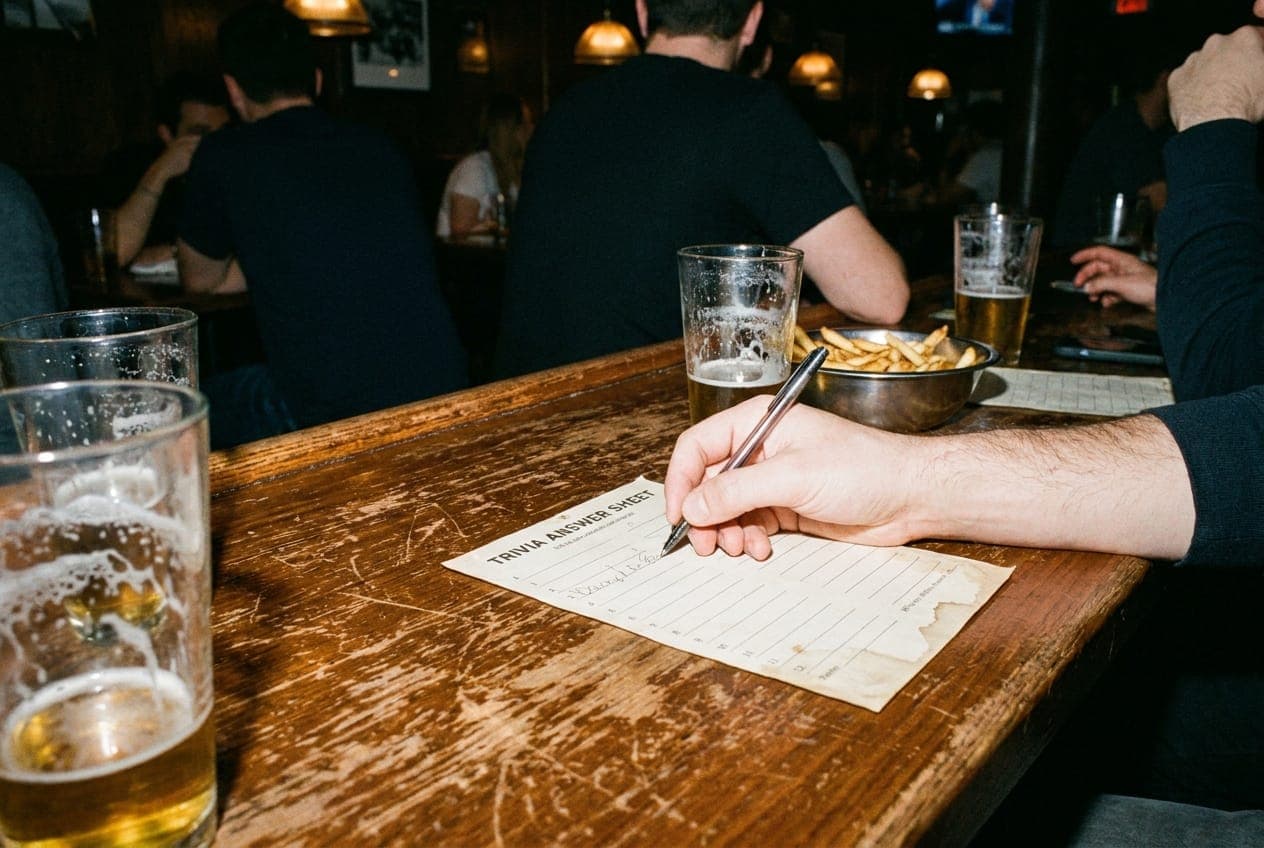 A group of friends laughing and holding beers around a table with a trivia answer sheet.
