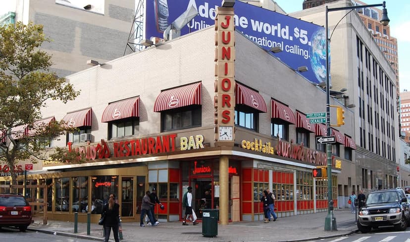 Exterior view of Junior's Restaurant at a street corner in Downtown Brooklyn, featuring red and white striped awnings.