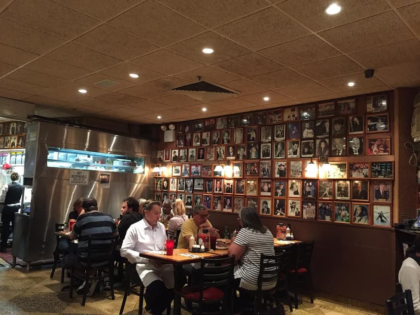 Interior of Carnegie Deli showing a wall covered with framed photos, diners at tables, and a stainless steel counter.