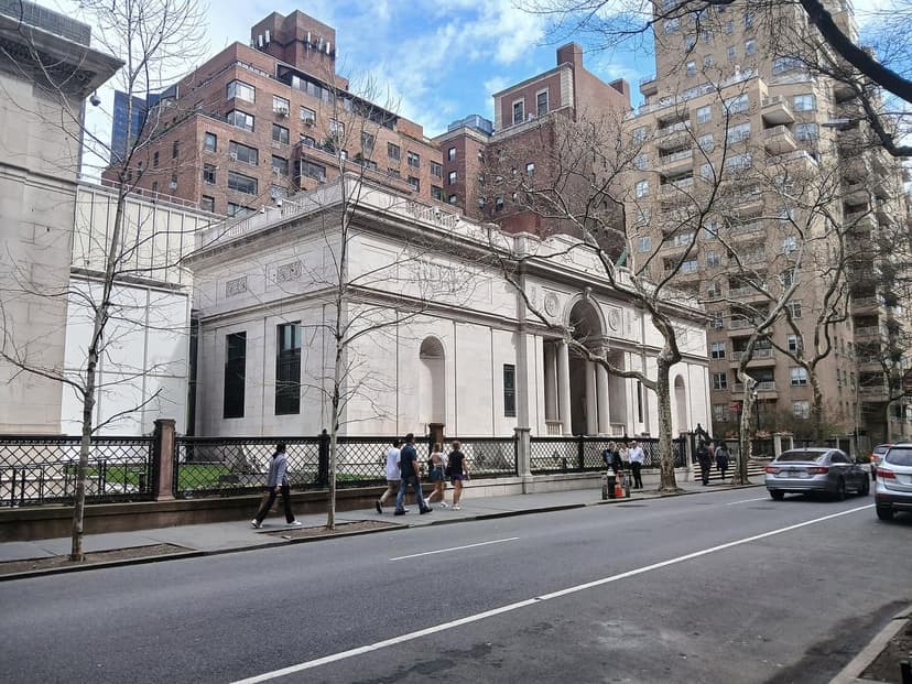 Exterior of the Morgan Library & Museum, a classical building with columns, on a city street with pedestrians and cars.