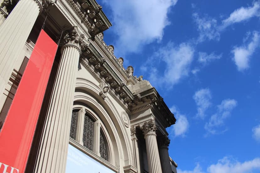 Low angle view of the exterior of a grand building with classical columns and ornate details, a red banner hangs on a column, under a blue sky