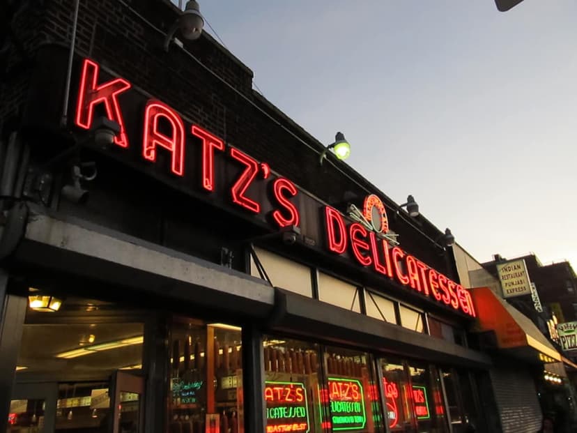 Exterior view of Katz's Delicatessen in Manhattan, New York, featuring its bright red neon sign against a twilight sky.