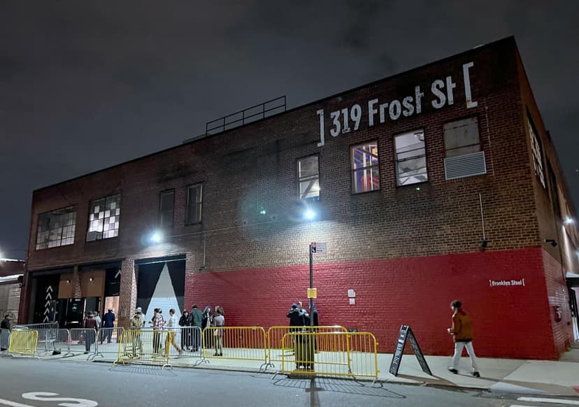 Exterior view of Brooklyn Steel at night, showing the brick building with '319 Frost St' and 'Brooklyn Steel' signs, and people queuing