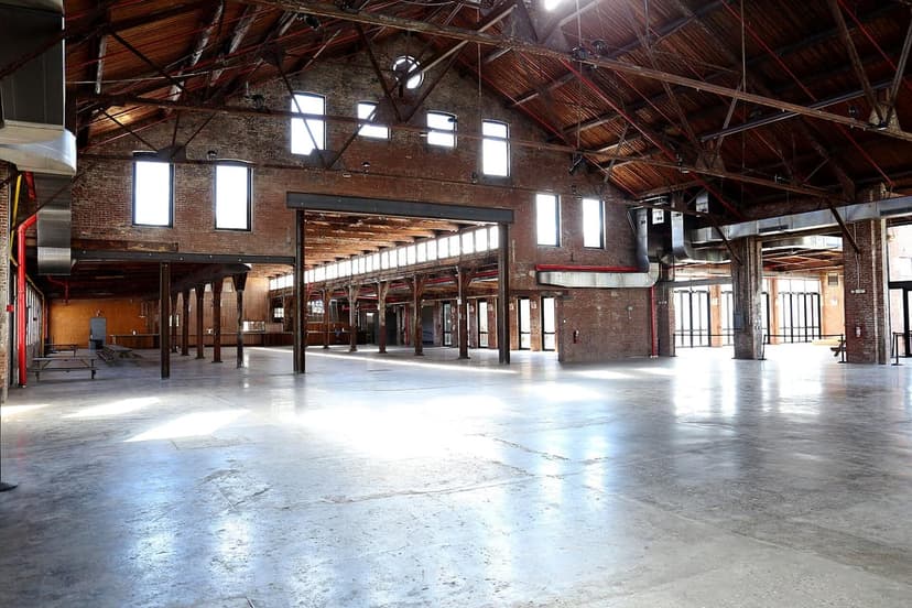 Interior of a large, empty industrial venue with high wooden ceilings, exposed brick walls, and concrete floors.