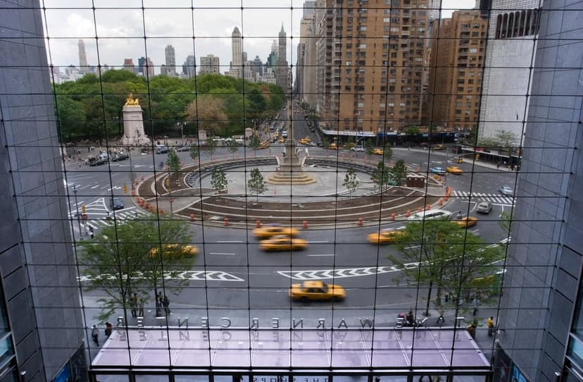 An aerial view of Columbus Circle in New York City, showing a circular intersection with a monument, yellow taxis, and surrounding