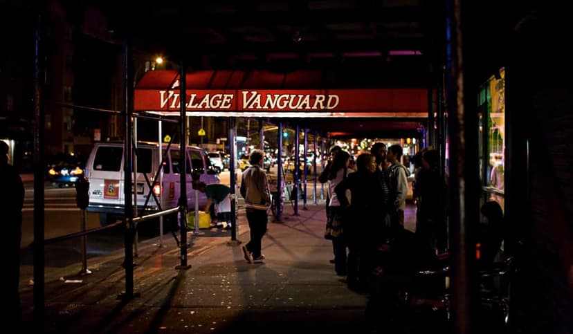 Village Vanguard jazz club exterior at night with a red awning and people waiting on the sidewalk.