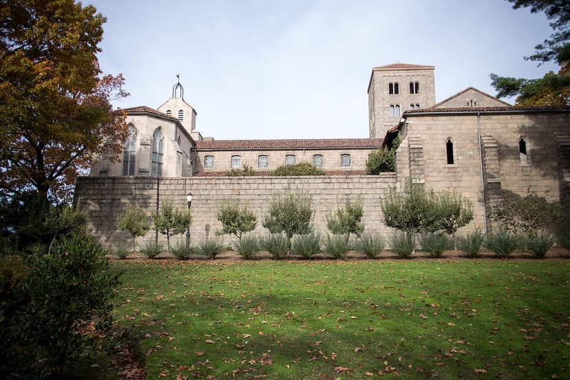 Exterior view of The Met Cloisters showing stone architecture, a bell tower, and surrounding gardens with trees and grass.