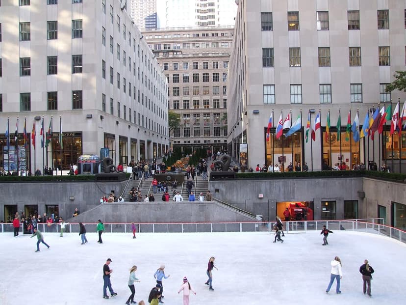 An aerial view of the ice skating rink at Rockefeller Center in New York City, with people skating and surrounding buildings.