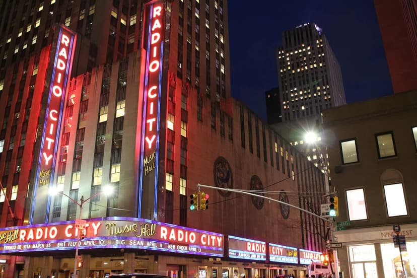 Exterior view of Radio City Music Hall at night, with red and blue neon signs illuminated.
