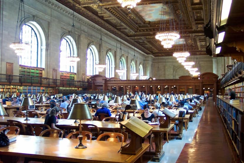 A wide view of the New York Public Library's Rose Main Reading Room, with many people at long wooden tables under chandeliers.