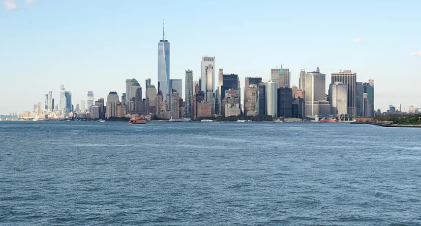 Manhattan skyline with One World Trade Center and other skyscrapers seen from the water, with an orange ferry boat.