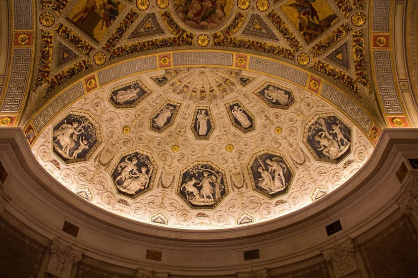 The ornate domed ceiling of the Morgan Library & Museum Rotunda, featuring intricate relief sculptures and painted details.
