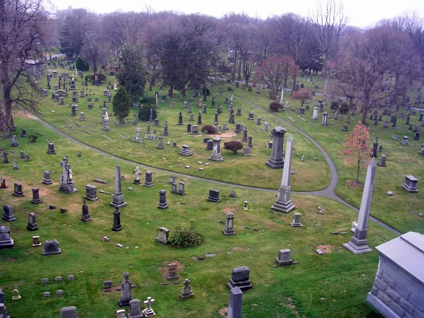 An aerial view of Green Wood Cemetery shows a vast green landscape dotted with numerous gravestones, monuments, and bare trees.