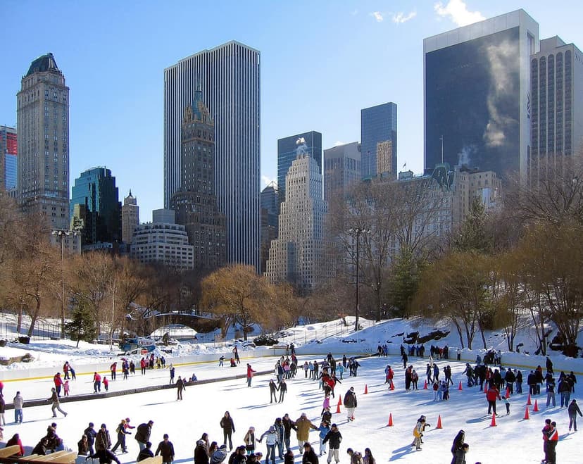 An aerial view of Wollman Rink in Central Park, New York City, with many people ice skating on a sunny winter day.