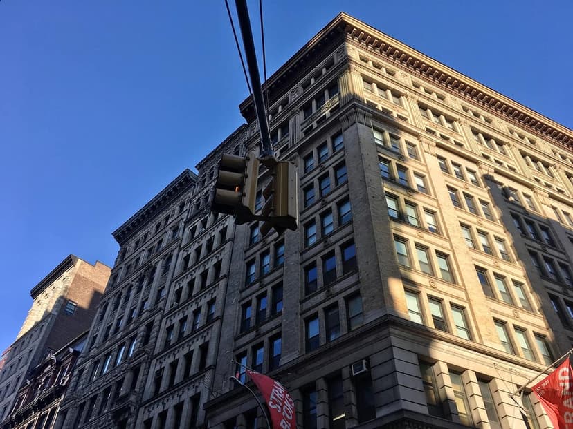 A tall, ornate building with many windows under a blue sky. A traffic light and a red flag for Strand Books are visible.