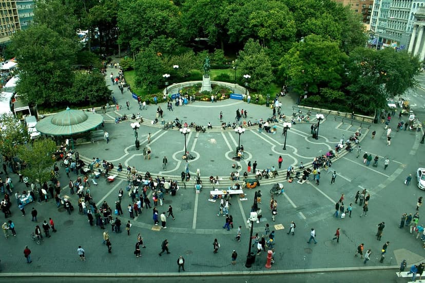 An aerial view of Union Square Park in New York City, showing many people, trees, and market stalls on a paved area.