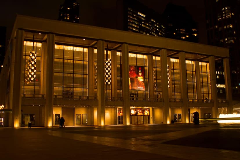 Exterior view of the David H. Koch Theater at Lincoln Center at night, with illuminated windows and columns.