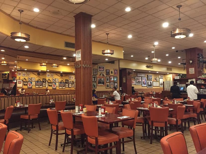 Interior of a restaurant with orange chairs, striped booths, and framed pictures on the walls and a central wooden column.