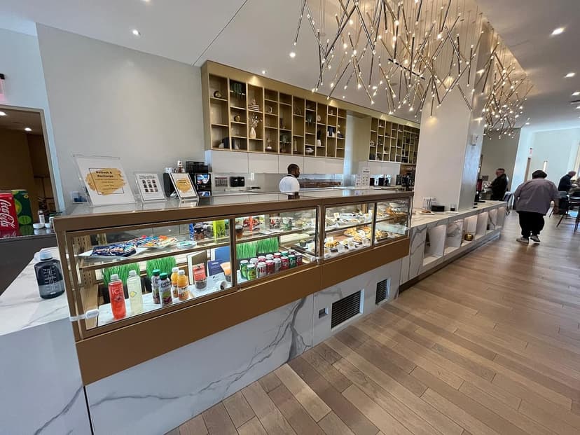 A food service counter with a display case of pastries and drinks, a long marble counter, and distinctive ceiling lights in a modern