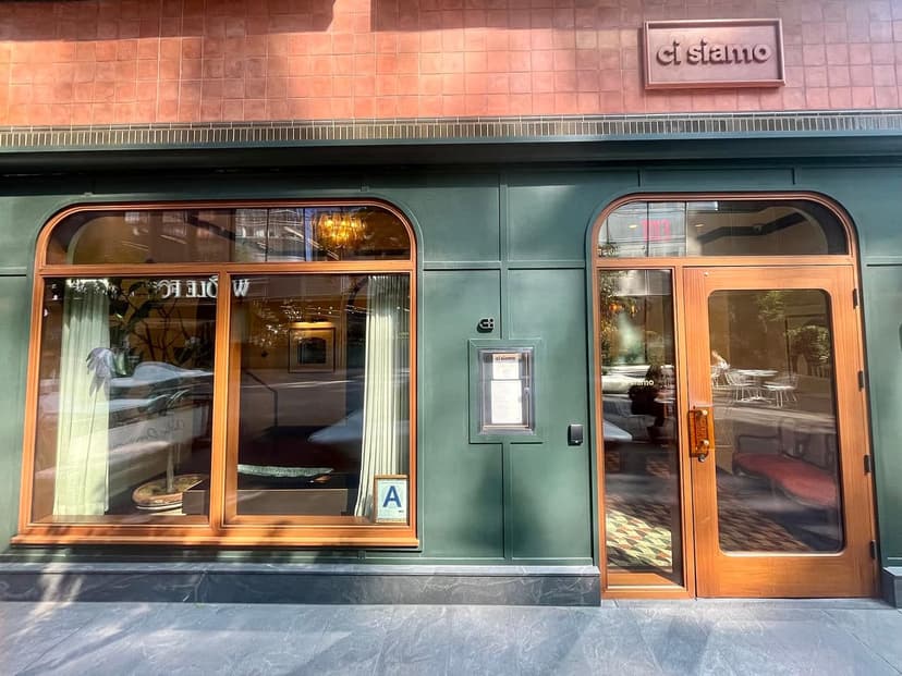 The exterior of Ci Siamo restaurant featuring a dark green facade, large wooden windows, and a wooden double door. A sign reads 'ci