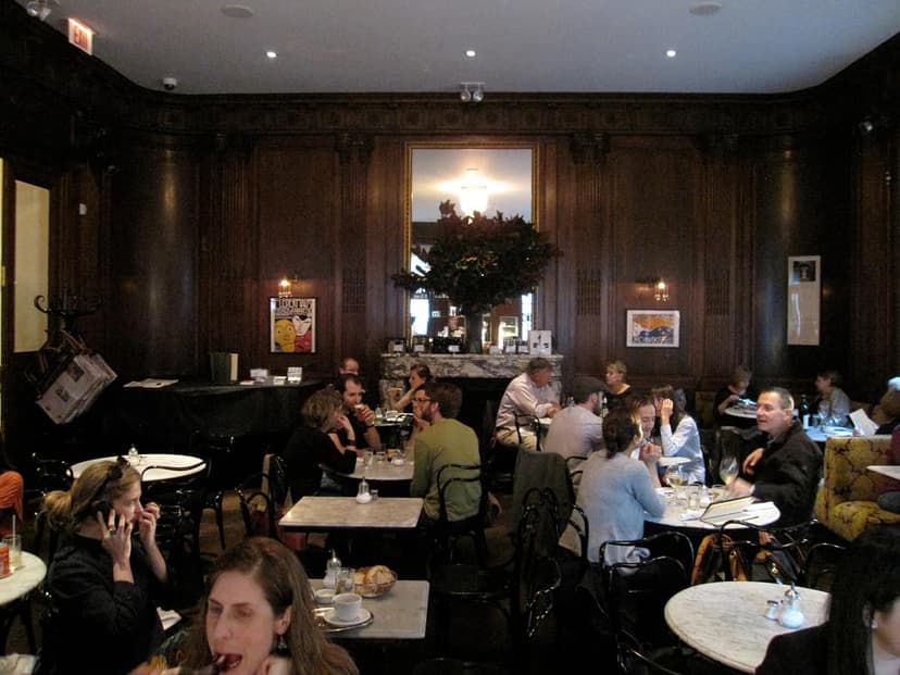 Interior view of a cafe with dark wood paneling, marble tables, and people dining and conversing.