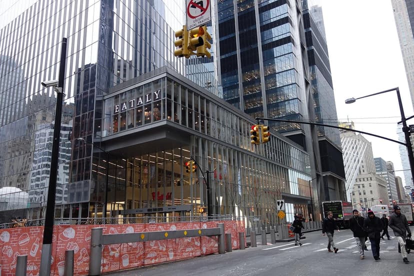 The Eataly sign on a modern glass building, 4 World Trade Center, with traffic lights and pedestrians on a city street.