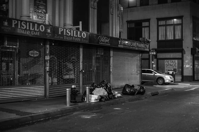 Black and white night photo of the Pisillo Italian Cafe and Panini storefront with closed metal gates, street, and trash bags.
