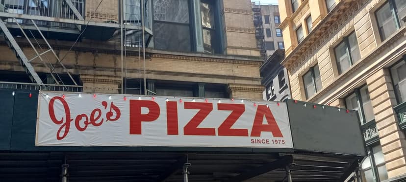 A white banner with red text reading 'Joe's PIZZA SINCE 1975' hangs on scaffolding in front of a building.
