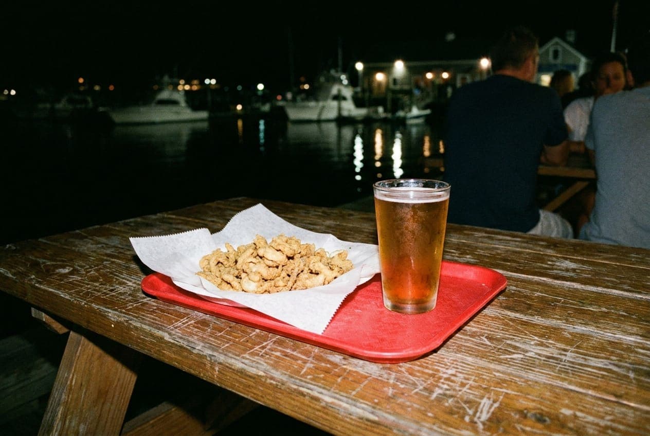A tray of fried clams and a cold beer on a picnic table overlooking the Long Island Sound at night.