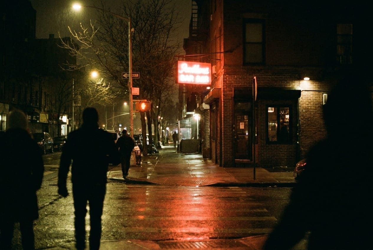 A neon sign glows outside a bar on a quiet Cobble Hill corner at night.