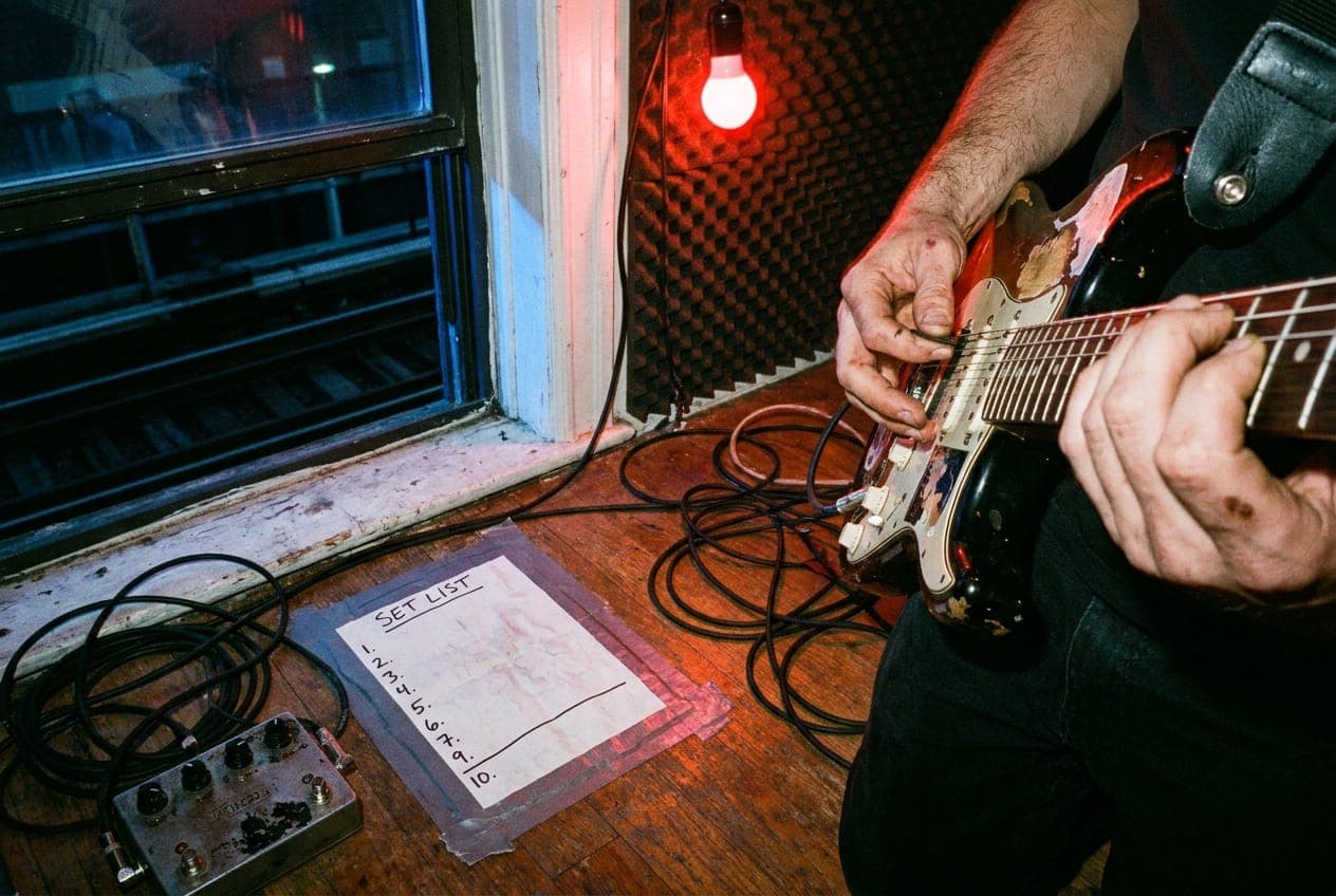 A crowded basement show seen from the back of the room, stage lights cutting through haze