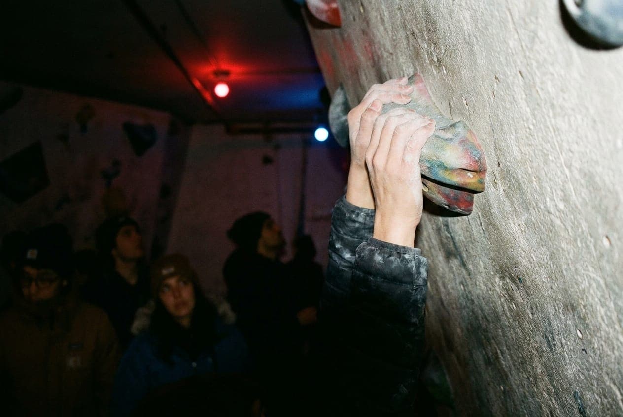 A close up of chalk-covered hands gripping a climbing hold on a textured indoor rock wall